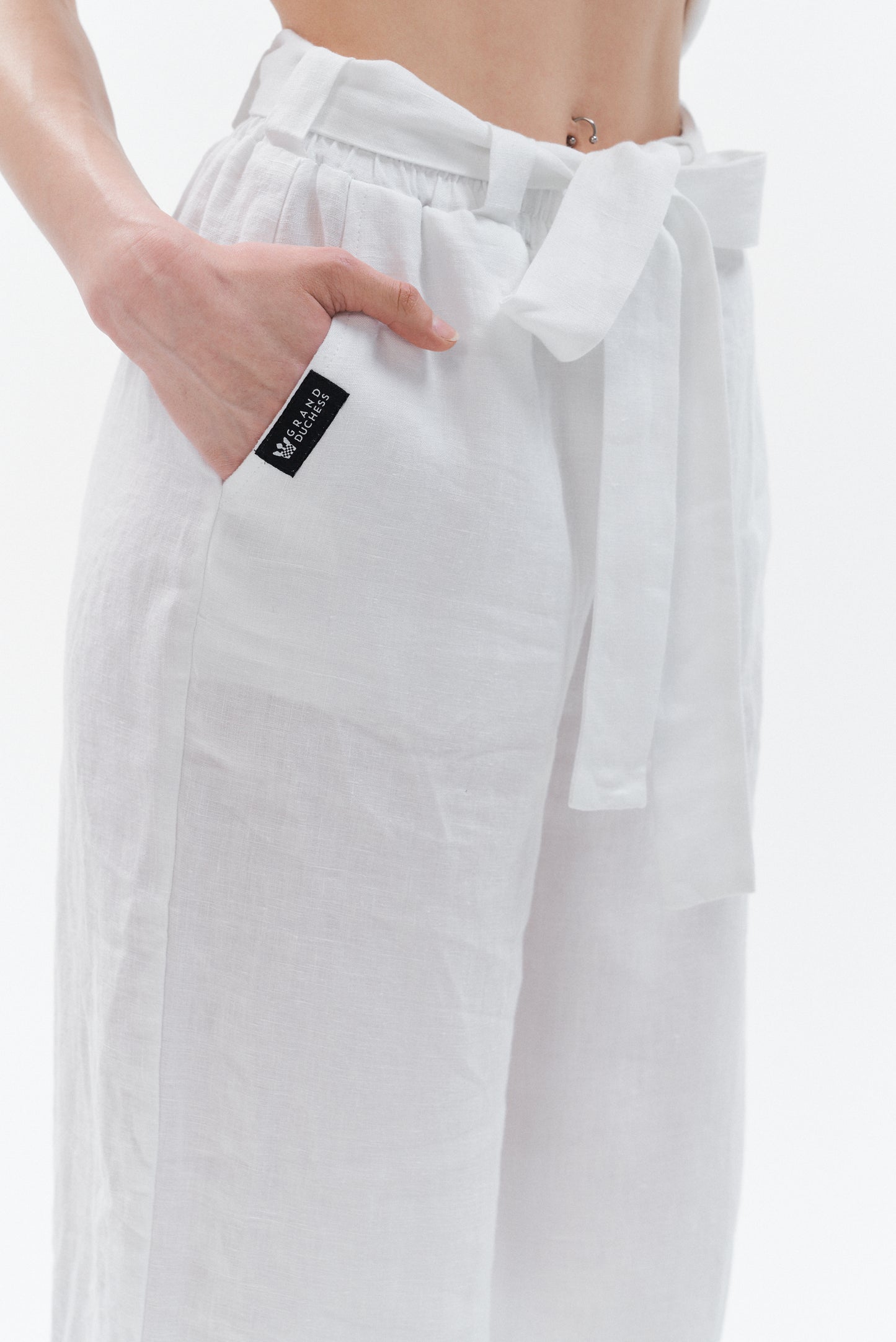 Close-up of women’s white linen pants showing elastic waistband, belt, and deep side pocket.