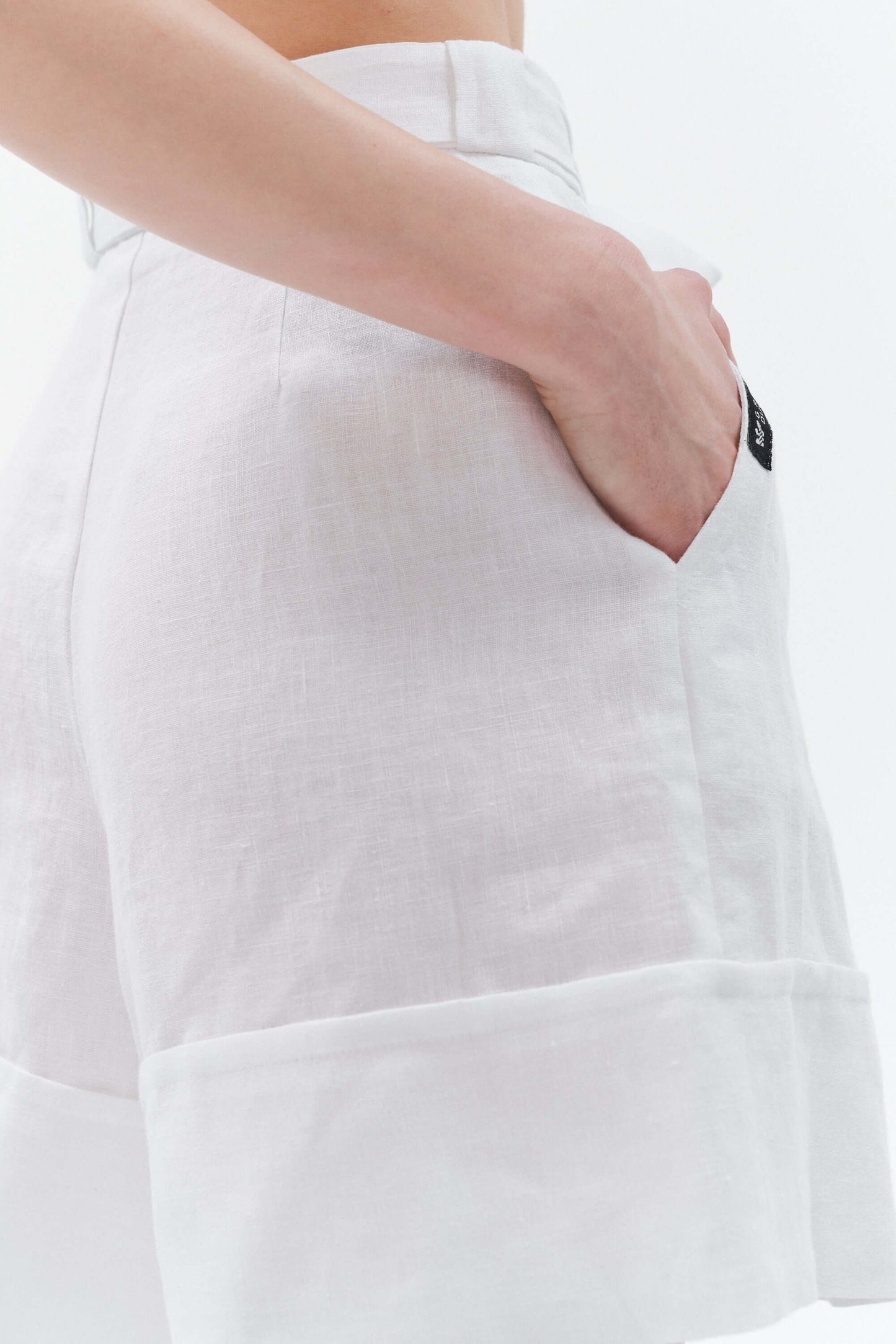 Close-up view of white Bonita wide-leg linen shorts showing subtle cotton logo label, matching linen belt, waist coverage and textured linen fabric.