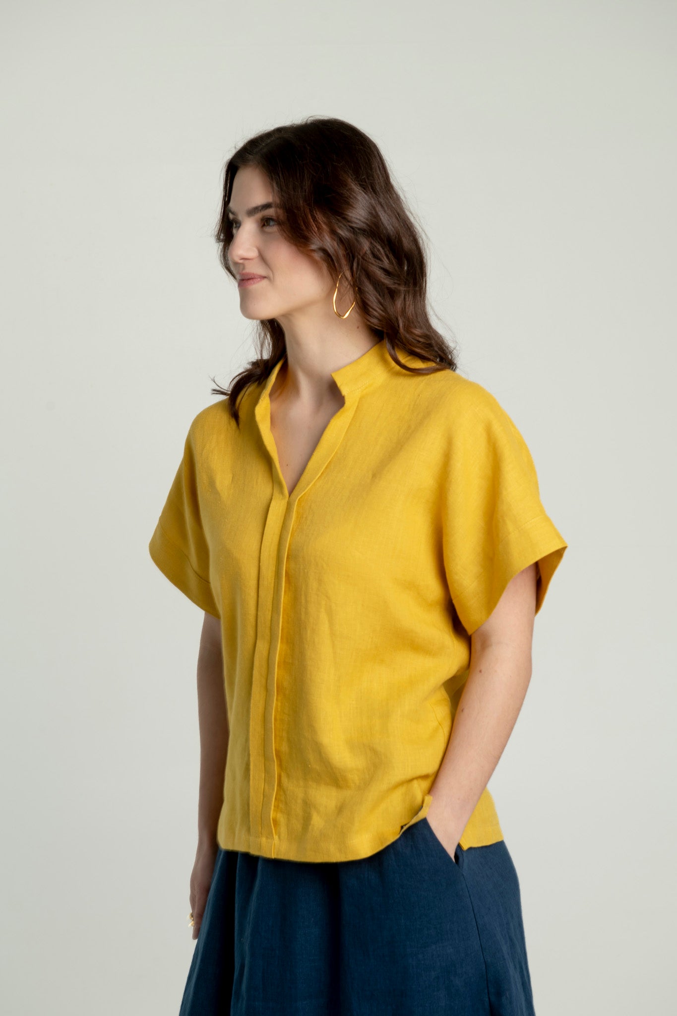 Semi side view of a woman wearing a mustard yellow Japanese style linen top with short sleeves and a V-neck collar.