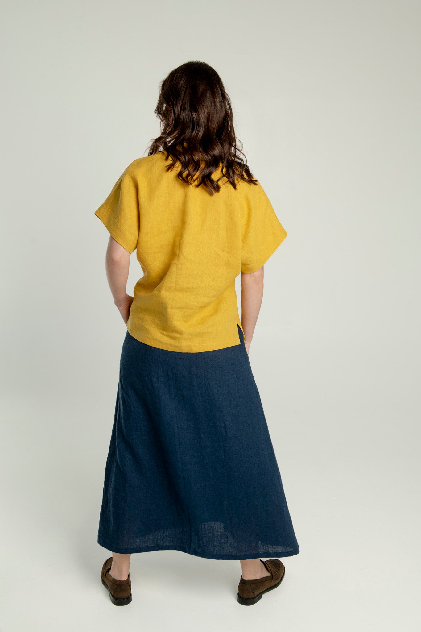 Back side view of a woman wearing a mustard yellow Japanese style linen top with short and wide sleeves.