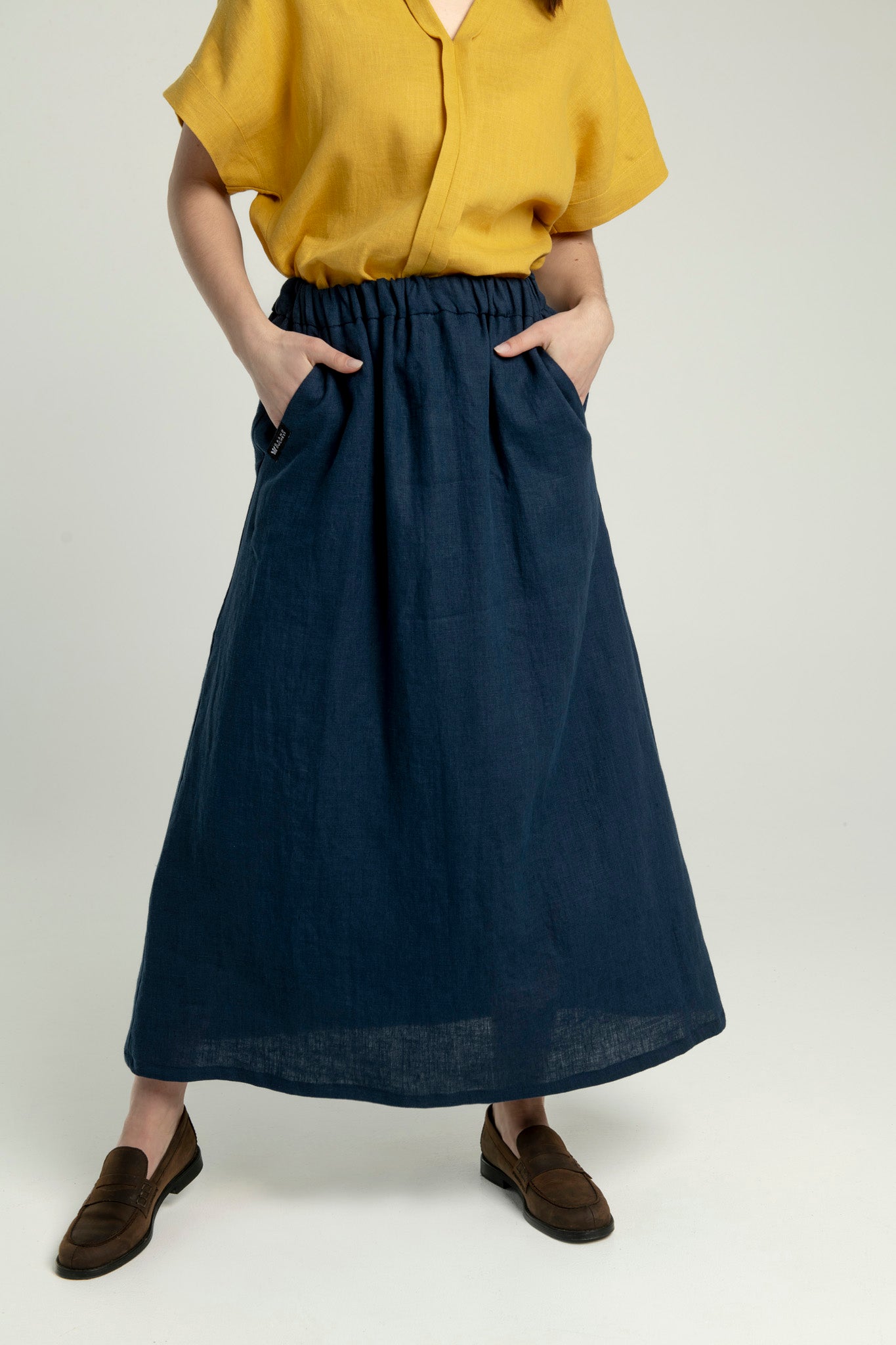 Close-up of a woman wearing a Soho navy blue maxi linen skirt with pockets, standing in a wide-leg pose with hands in pockets.