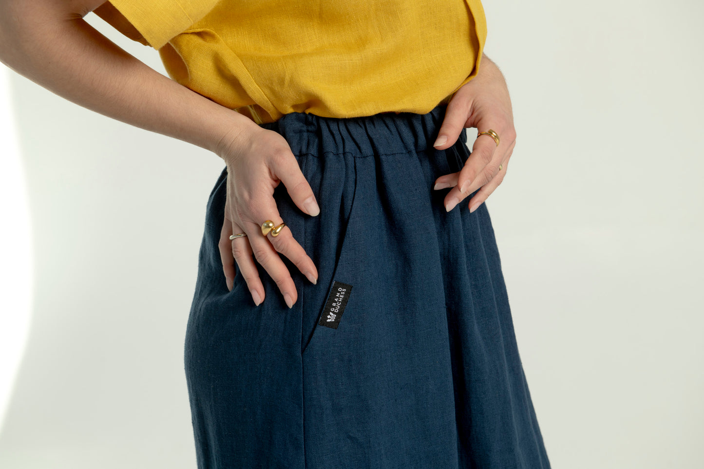 Close-up side view of a woman wearing a Soho navy blue maxi linen skirt with pockets, highlighting the logo detail on the pocket.