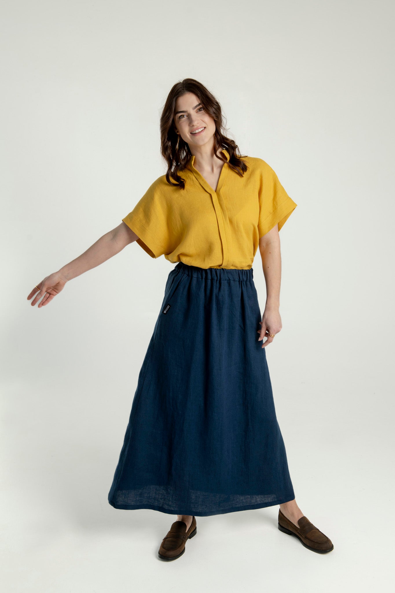 Front view of a woman wearing a mustard yellow Japanese style linen top with short and wide sleeves and a V-neck collar, styled with a navy blue long linen skirt Soho.