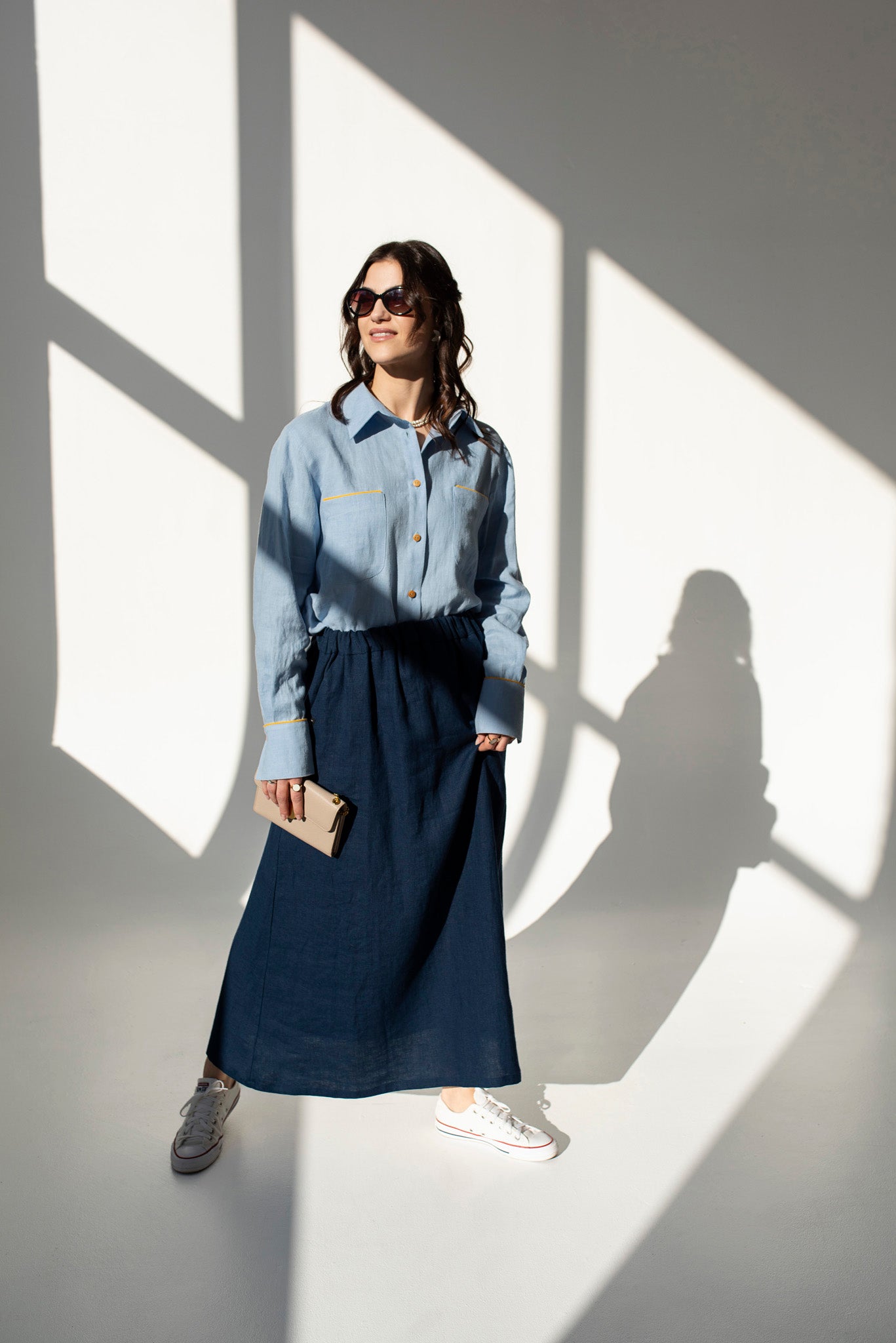Front view of woman wearing a navy blue linen maxi skirt Soho with side pockets and elastic waistband, styled for an elegant urban look, standing in a room with dappled light.