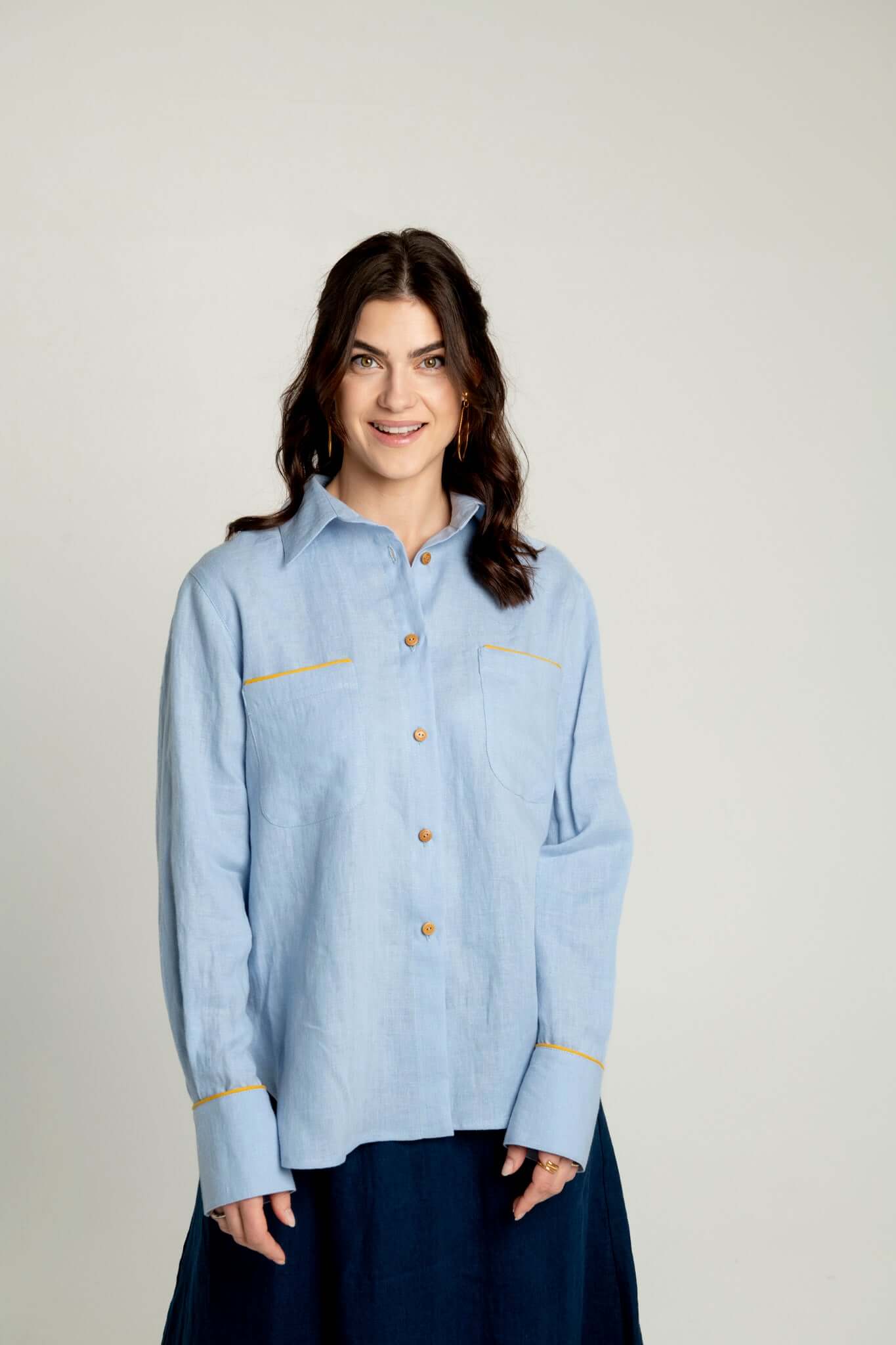 Woman wearing a light blue denim shirt with yellow accents on a plain background