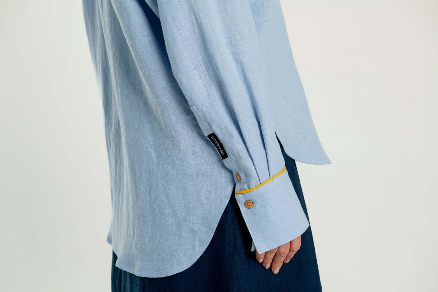 The long sleeve details of light blue linen shirt with a yellow details on a plain background