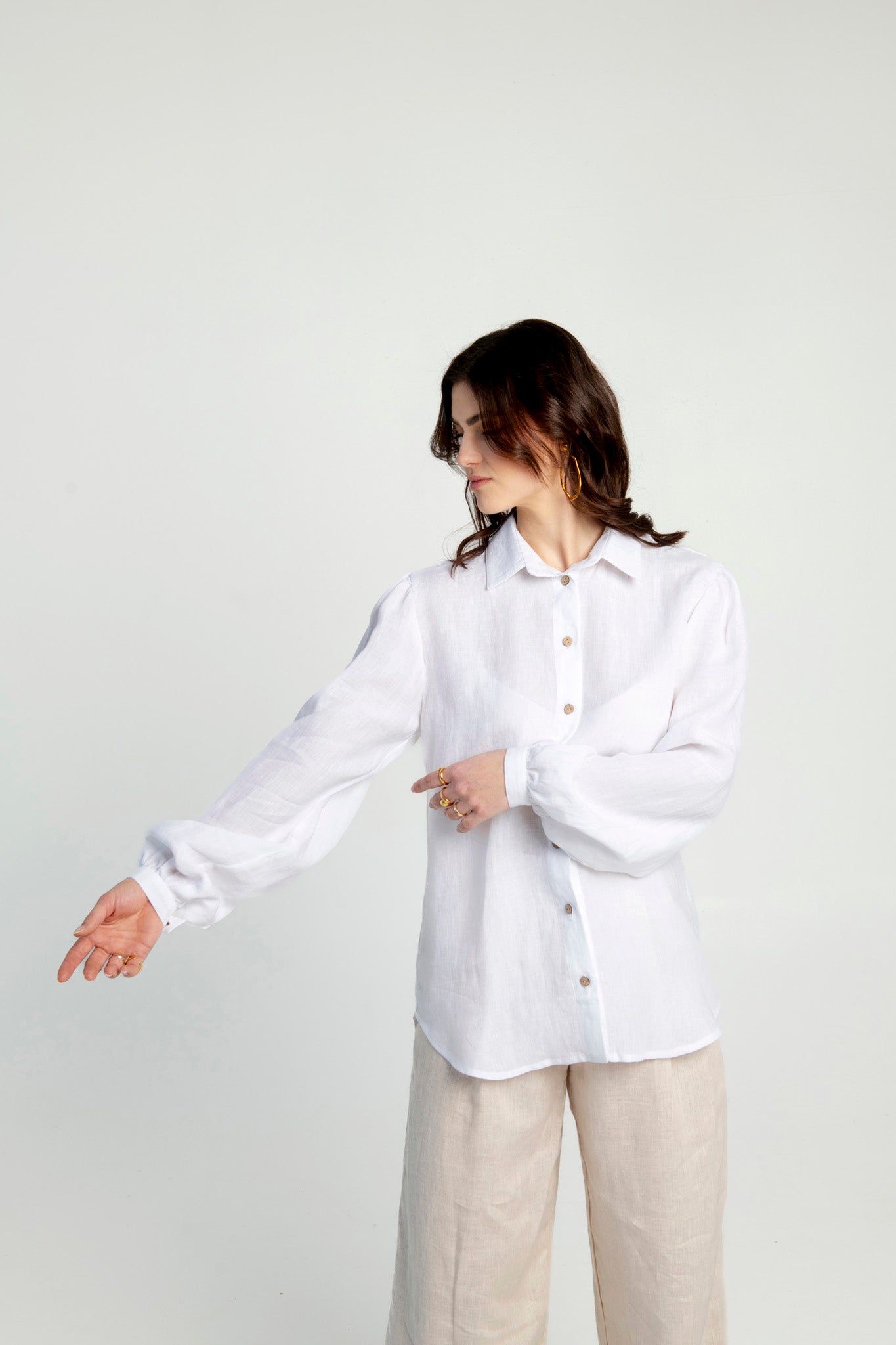 Front side of women wearing white and lightweight linen shirt with puffed sleeves Astoria with a beige linen pants. Women is showing how elegant looks puffed sleeves of linen shirt Astoria.