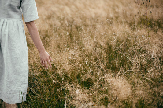 A woman in sustainable linen clothing walks through a grassy field, showcasing eco-friendly fashion in Lithuania.