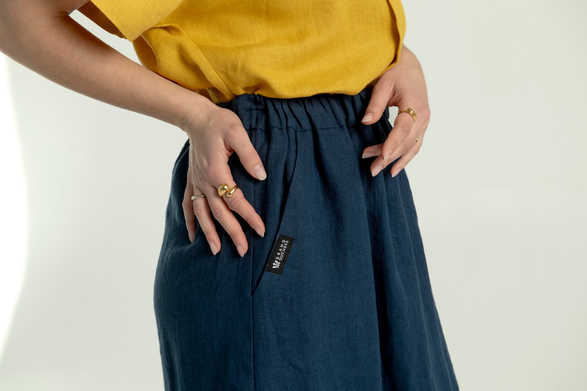 Close-up side view of a woman wearing a Soho navy blue maxi linen skirt with pockets, highlighting the logo detail on the pocket.