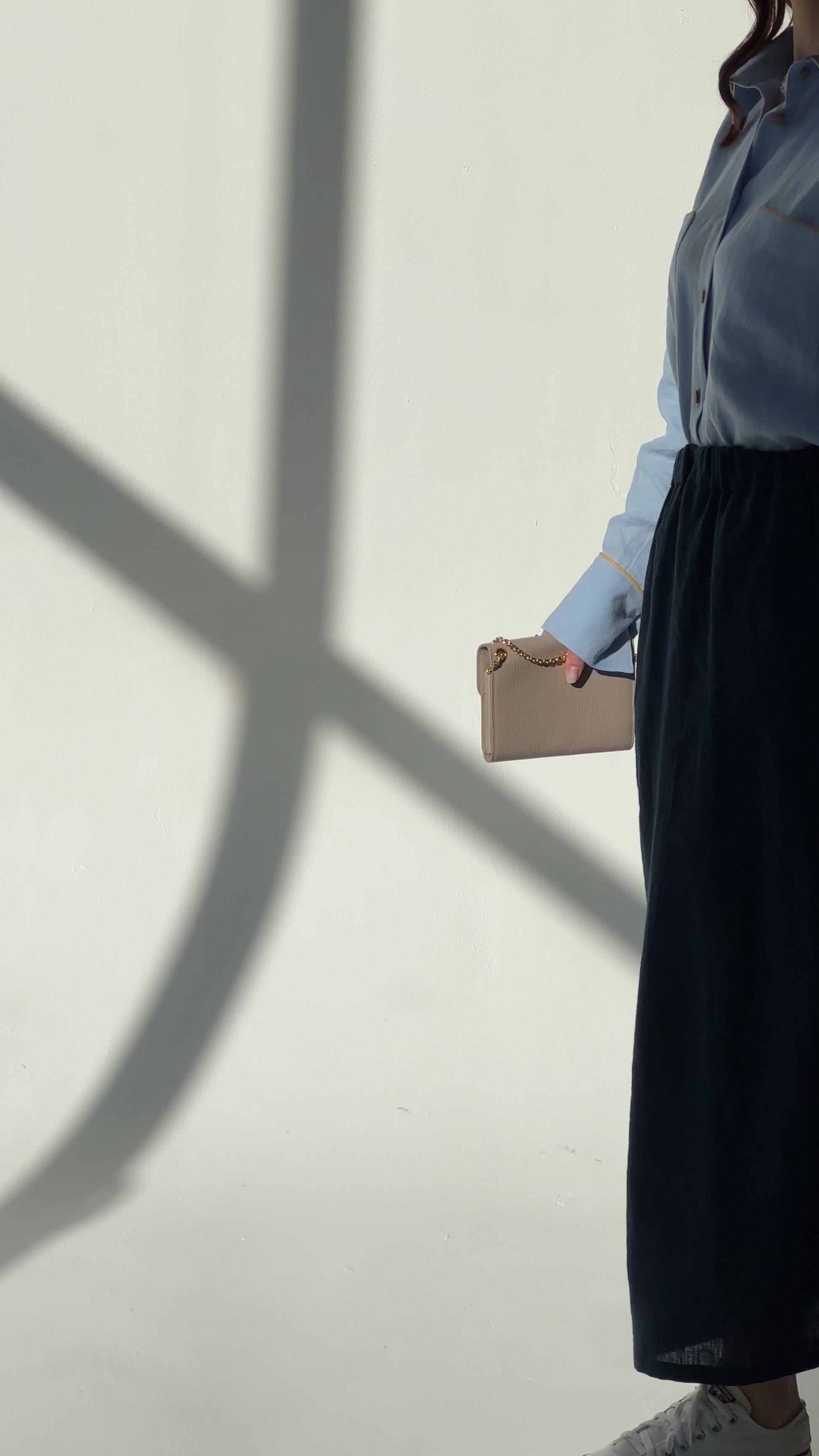 Video of a woman wearing a navy blue linen maxi skirt Soho with side pockets and elastic waistband, styled for an elegant urban look, moving slowly in a room with dappled light.
