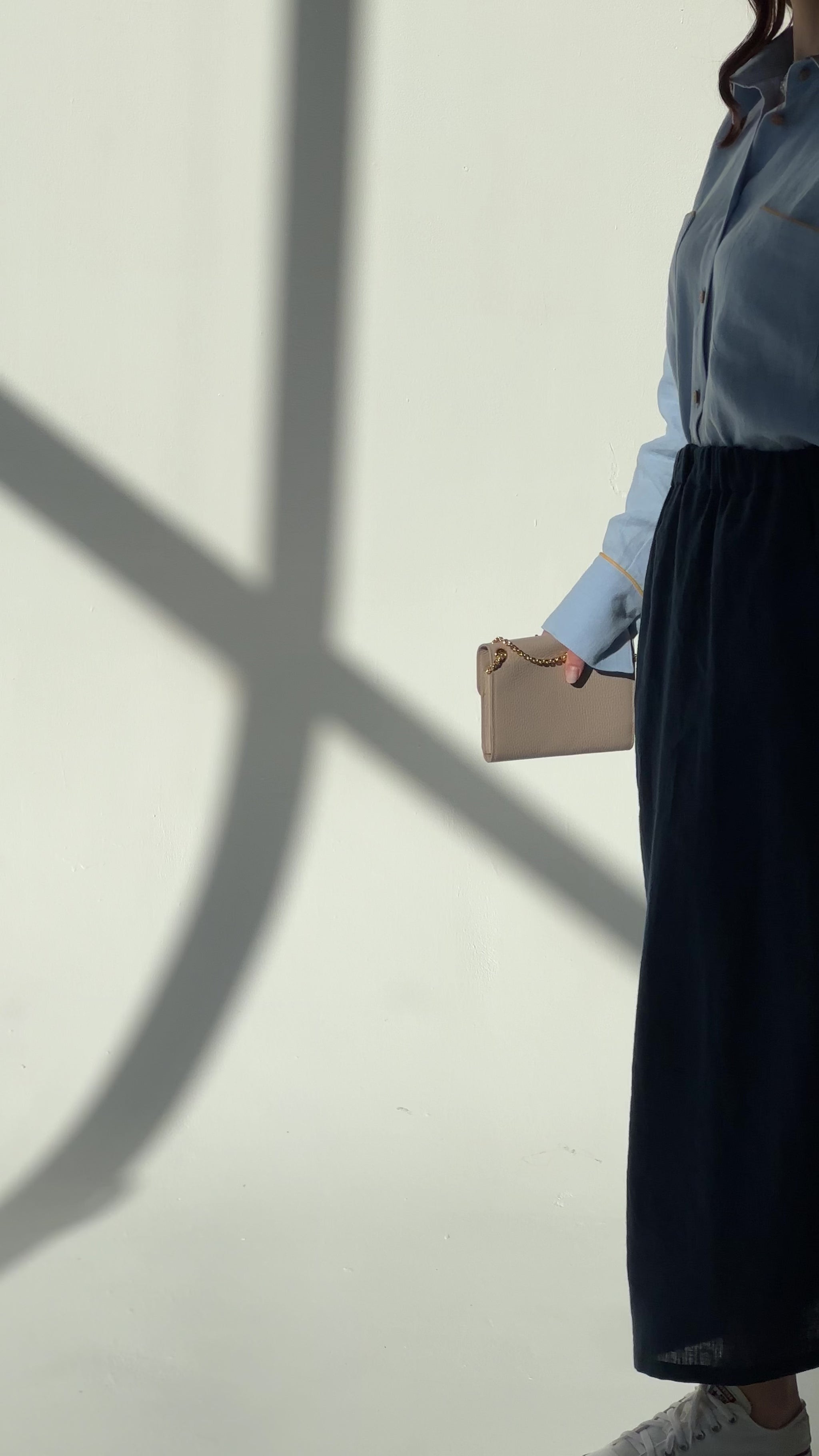 Video of a woman wearing a navy blue linen maxi skirt Soho with side pockets and elastic waistband, styled for an elegant urban look, moving slowly in a room with dappled light.